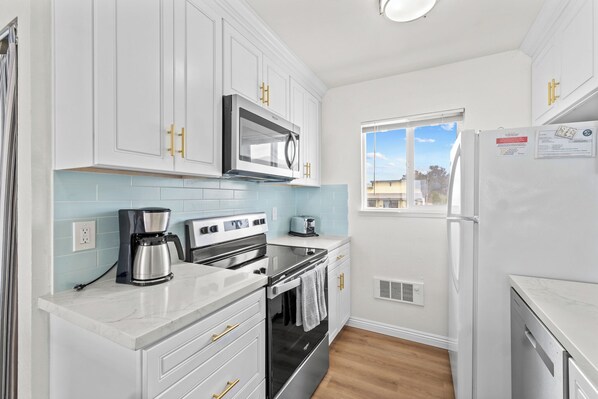 A modern kitchen with white cabinets, stainless steel appliances, and a window providing natural light.