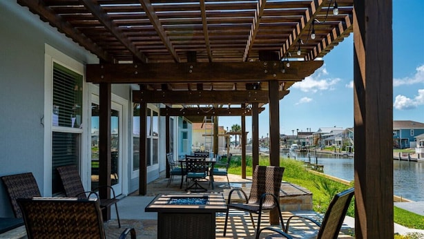 A covered patio with outdoor furniture, a view of a canal, and a building with windows. - It`s clock out time! (Rockport)