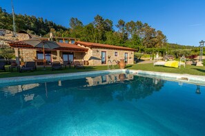 Un espace piscine agrémenté d’une maison en pierre, de mobilier d’extérieur et d’un ciel dégagé.