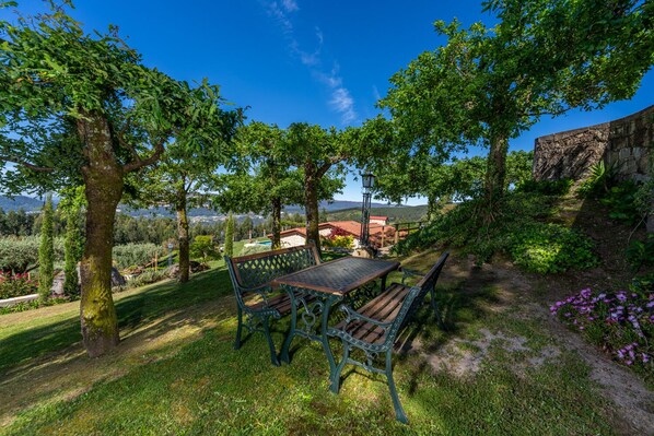 Un jardin avec une table et des bancs, entouré d’arbres et offrant une vue sur un paysage lointain.