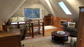 Un dormitorio acogedor en el ático con cama tipo loft, un escritorio, una silla, una mesita, un sofá y una estantería.