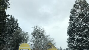 Paisaje rural cubierto de nieve con un granero amarillo y un edificio más pequeño con una puerta blanca.