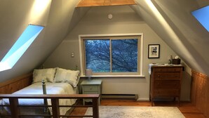 Un dormitorio acogedor en el ático con un ventanal grande, una cama, una mesita de noche, un aparador y un banco de madera.