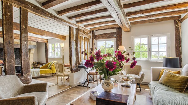 Amplia sala de estar con vigas de madera a la vista, un sofá, una mesa de centro y un florero con flores.