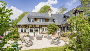 Una casa de dos pisos con fachada de piedra, múltiples ventanas y un patio con mobiliario exterior.