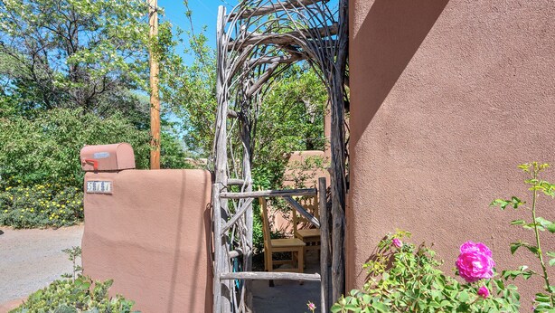 A rustic gate with a mailbox, a wooden bench, and a cactus garden. - Mariposa | Charming Adobe Home in Santa Fe (Santa Fe)