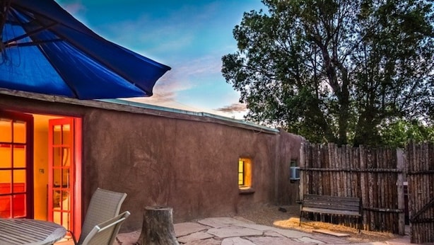 A patio with stone flooring, a wooden table, chairs, a blue umbrella, and a rustic wooden fence.