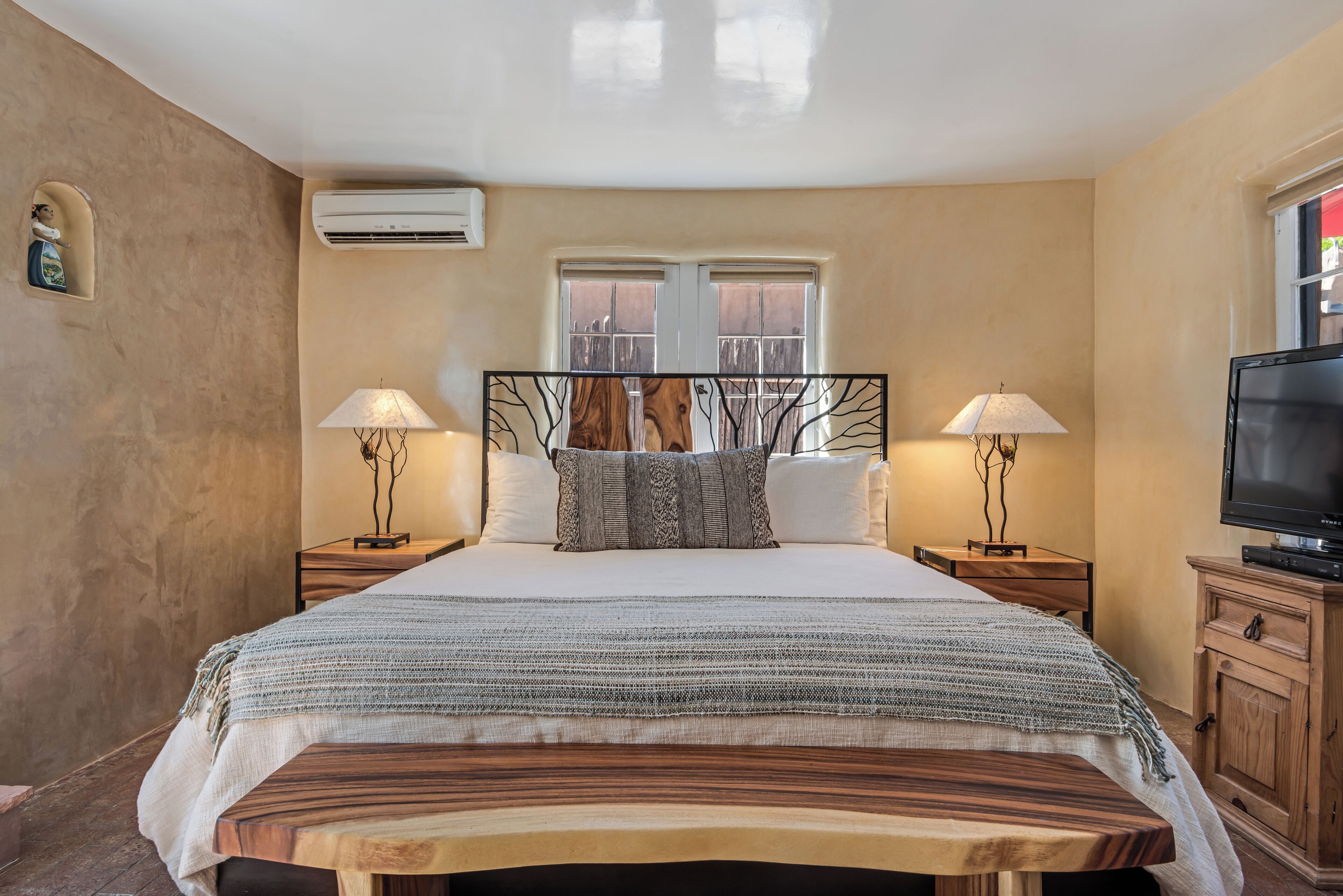 A bedroom with a large bed, two bedside tables with lamps, a TV, and a window with a view.