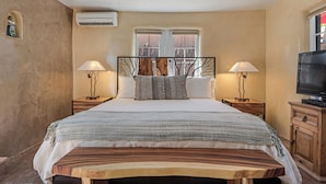A bedroom with a large bed, two bedside tables with lamps, a TV, and a window with a view.