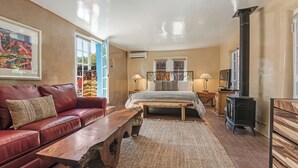 A cozy bedroom with a red leather sofa, a wooden bench, a large bed with a wooden headboard, and a black wood-burning stove.