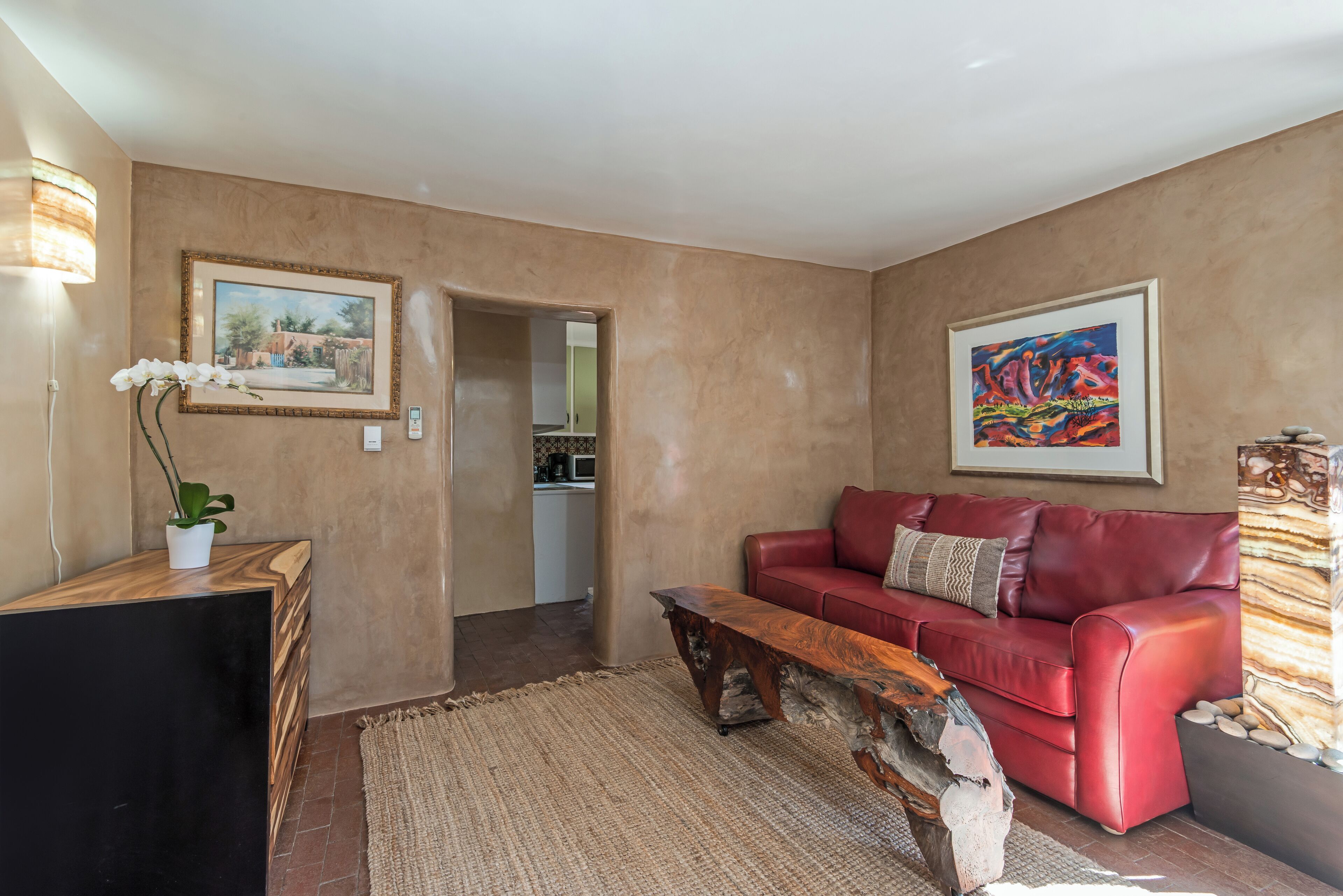 Un salon avec un canapé en cuir rouge, une table basse en bois et un tableau encadré accroché au mur.