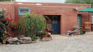 A rustic building with a blue door, surrounded by potted plants and a gravel driveway.