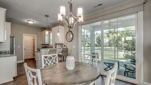 Una cocina amplia con armarios blancos, una mesa de comedor de madera y un ventanal con vistas al exterior.