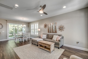 A spacious living room with a ceiling fan, a gray sofa, a coffee table, and a dining area with white chairs.