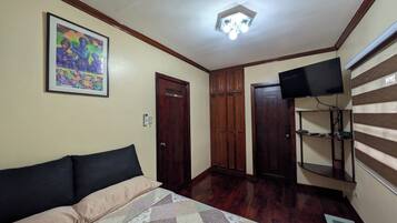 A bedroom with a bed, a TV mounted on the wall, and a wooden wardrobe.