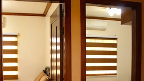 A room with a wooden floor, a bed with a patterned bedspread, a bedside table, and a window with blinds. - Entire House in Safe & Peaceful, Gated, Golf Community with 2 Swimming Pools. (General Trias)