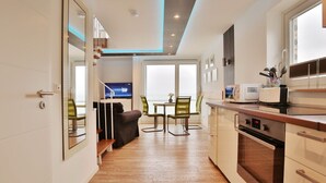 Een moderne keuken met een inbouwoven, een eethoek met tafel en stoelen, en een zithoek met een bank en een televisie.