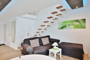 Uma sala de estar moderna com escada, conjunto de sofá e uma obra de arte com moldura verde na parede.