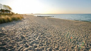 Een strand met een heldere lucht, een rustige zee en een brug in de verte.