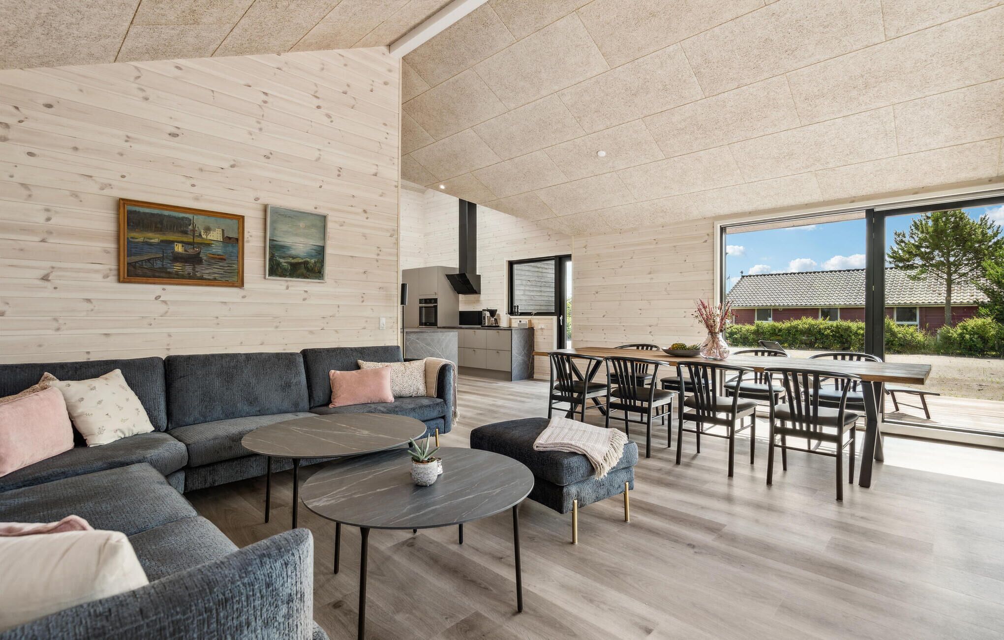 Un vaste espace de vie comprenant un canapé, une table basse et un ensemble de salle à manger. Les murs sont ornés de tableaux et l’on peut admirer la vue sur l’extérieur.