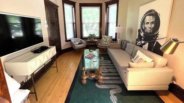 A modern living room with a flat-screen TV, a sofa, a coffee table, and a large window. - Irving Park/Avondale Updated Vintage Top Unit in 2-Flat (Chicago)