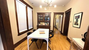 A dining area with a white table, black chairs, wooden flooring, and a wooden cabinet with glass doors. - Irving Park/Avondale Updated Vintage Top Unit in 2-Flat (Chicago)