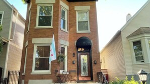 A two-story brick building with a black front door, windows, and a small outdoor seating area with a table and chairs. - Irving Park/Avondale Updated Vintage Top Unit in 2-Flat (Chicago)