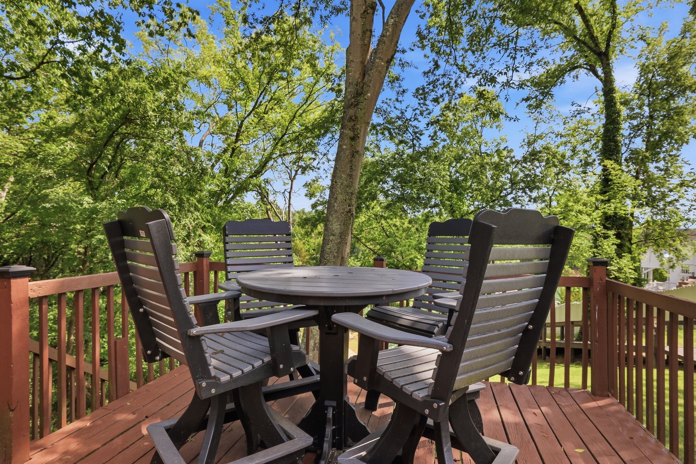 A deck with a round table and four chairs, surrounded by a wooden railing.