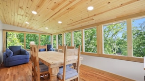 A room with a wooden ceiling, large windows, a wooden dining table, and a blue sofa. - 20% OFF NEW Dock, Pavilion, Hot Tub, Kayaks, Lakefront- Blue Heron Landing (Dandridge)
