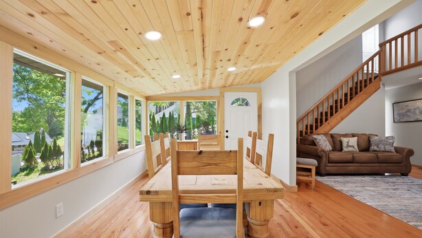 A dining area with a wooden table and chairs, large windows, a staircase, and a brown sofa. - 20% OFF NEW Dock, Pavilion, Hot Tub, Kayaks, Lakefront- Blue Heron Landing (Dandridge)