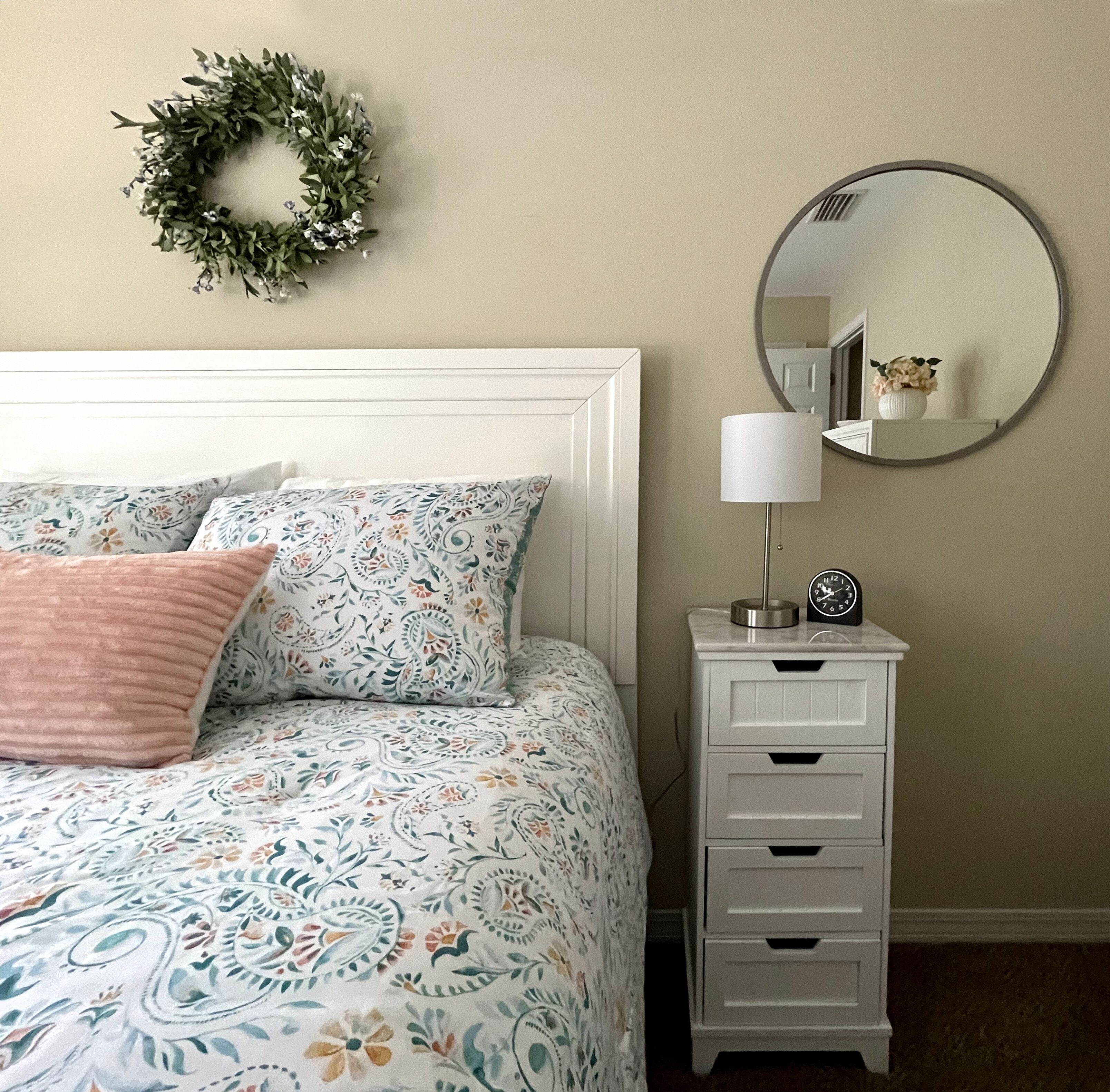 Un dormitorio con cama, mesita de noche, espejo y un arreglo decorativo en la pared.
