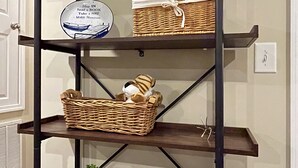 A three-tiered metal shelf unit with wicker baskets and a welcome sign.