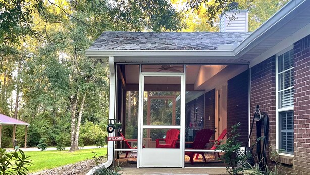 A covered porch with a welcome sign, red chairs, and a view of the surrounding greenery.