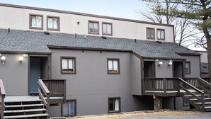 A two-story building with a flat roof, multiple windows, and a set of wooden stairs leading to a balcony.
