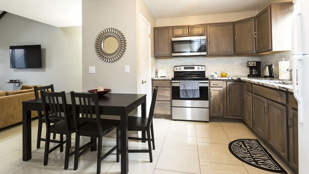 A modern kitchen with dark wooden cabinets, stainless steel appliances, and a dining area with a black table and chairs.
