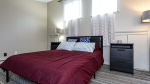 A bedroom with a large bed, a nightstand, a dresser, and a lamp.