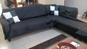 A sectional sofa with a dark fabric and white and black cushions, a wooden coffee table with a bowl of snacks, and a small sign on the table.