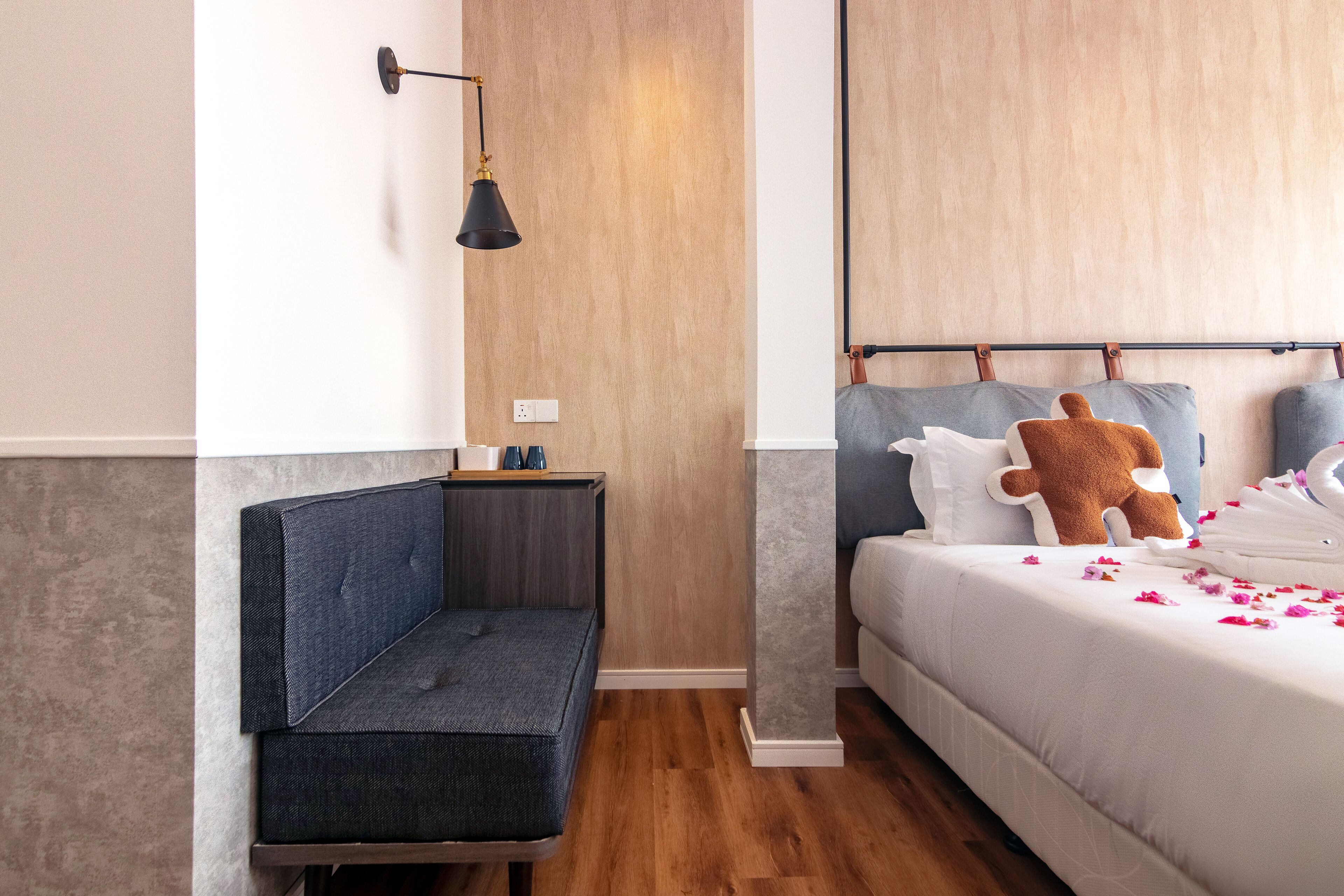 A modern hotel room with a bed, a bench, a nightstand, and a wall-mounted lamp.