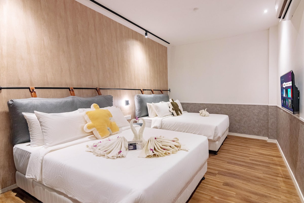 A hotel room with two beds, each with white linens and pillows, a wooden headboard, and a flat-screen TV on the wall.