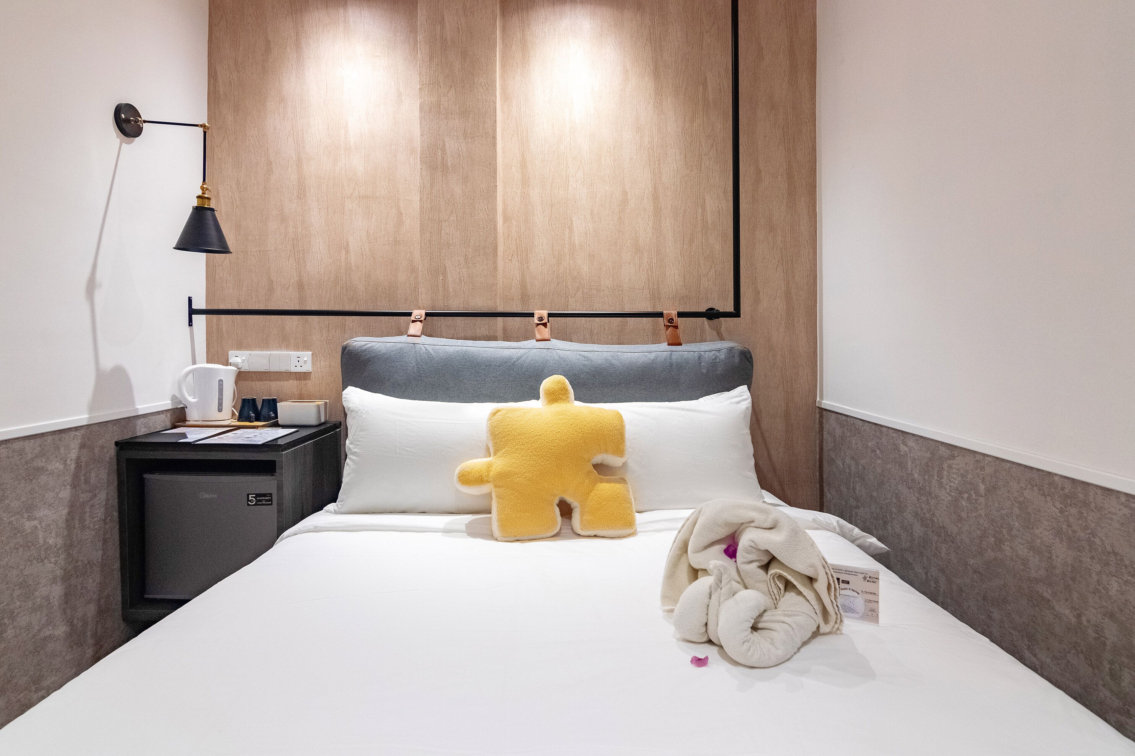 A hotel room with a bed, a nightstand, a lamp, and a plush toy.