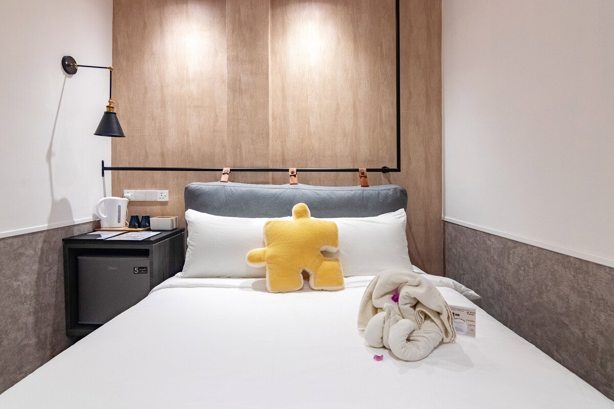 A hotel room with a bed, a nightstand, a lamp, and a plush toy.