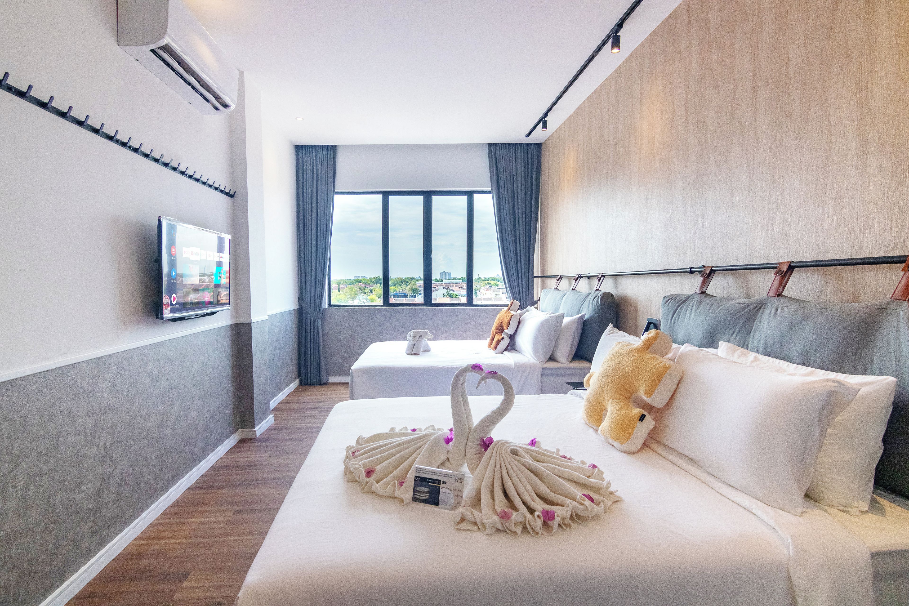 A hotel room with a bed, a TV, a window with curtains, and a view of the city.