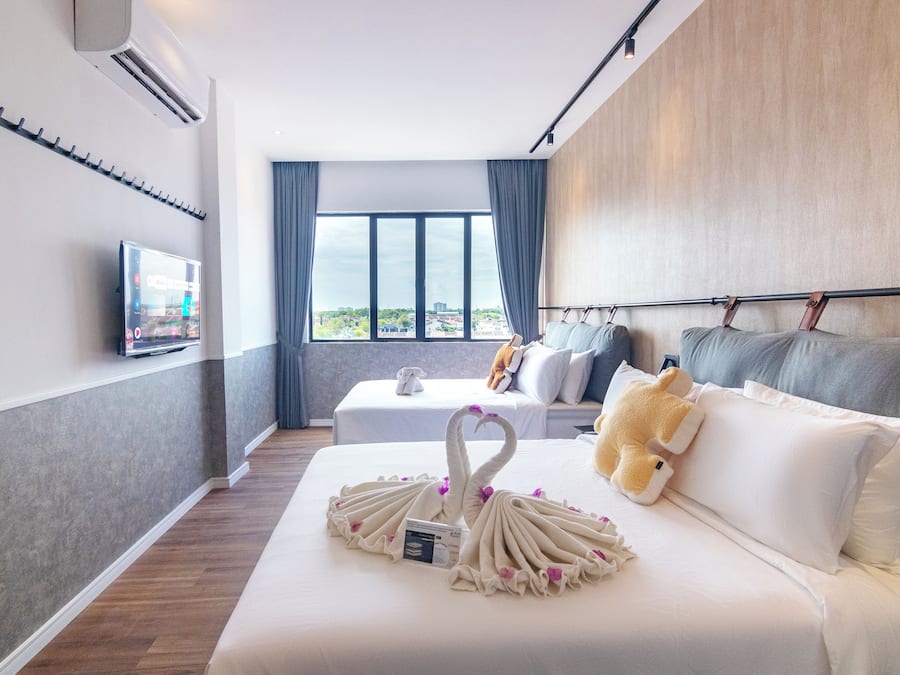 A hotel room with a bed, a TV, a window with curtains, and a view of the city.
