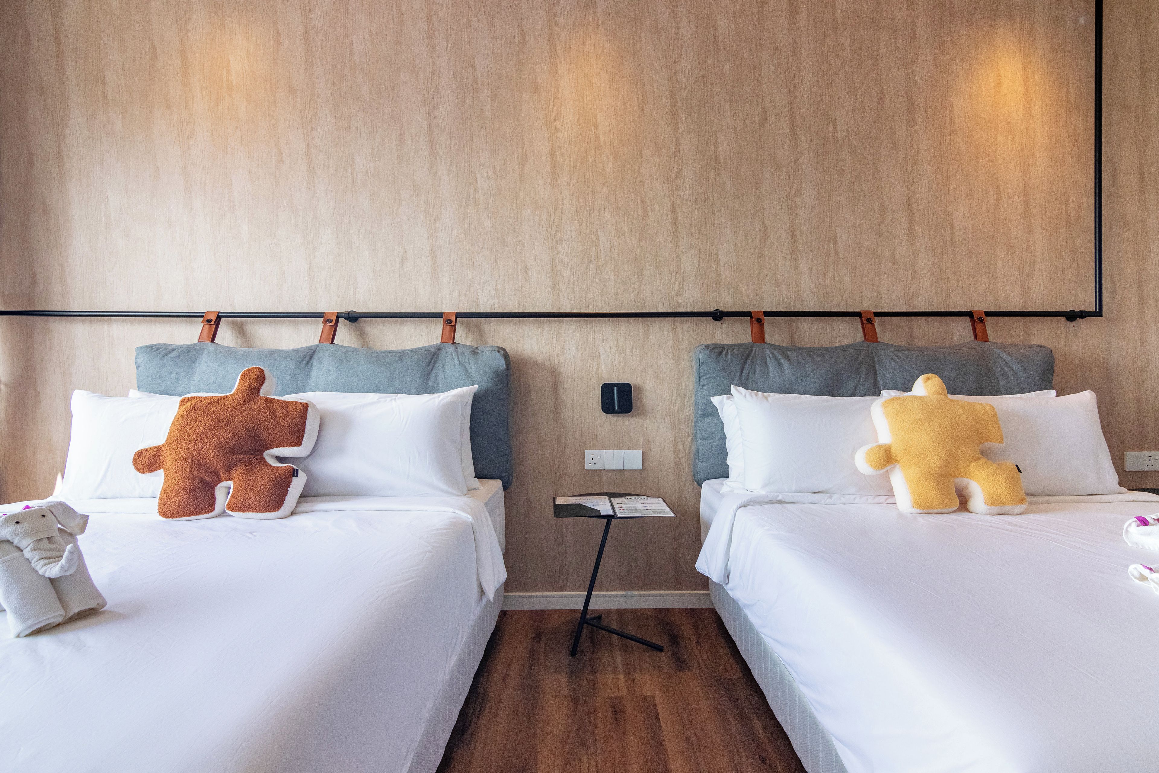 Une chambre d’hôtel avec deux lits, chacun agrémenté d’un ours en peluche, doté de draps blancs et muni d’une tête de lit en bois.