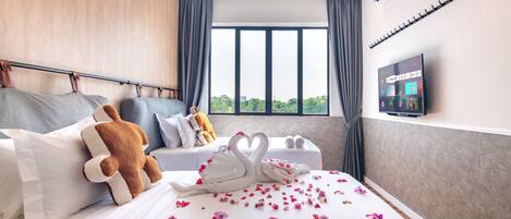 Habitación de hotel con cama, televisión, ventana con cortinas y vistas a zonas verdes.