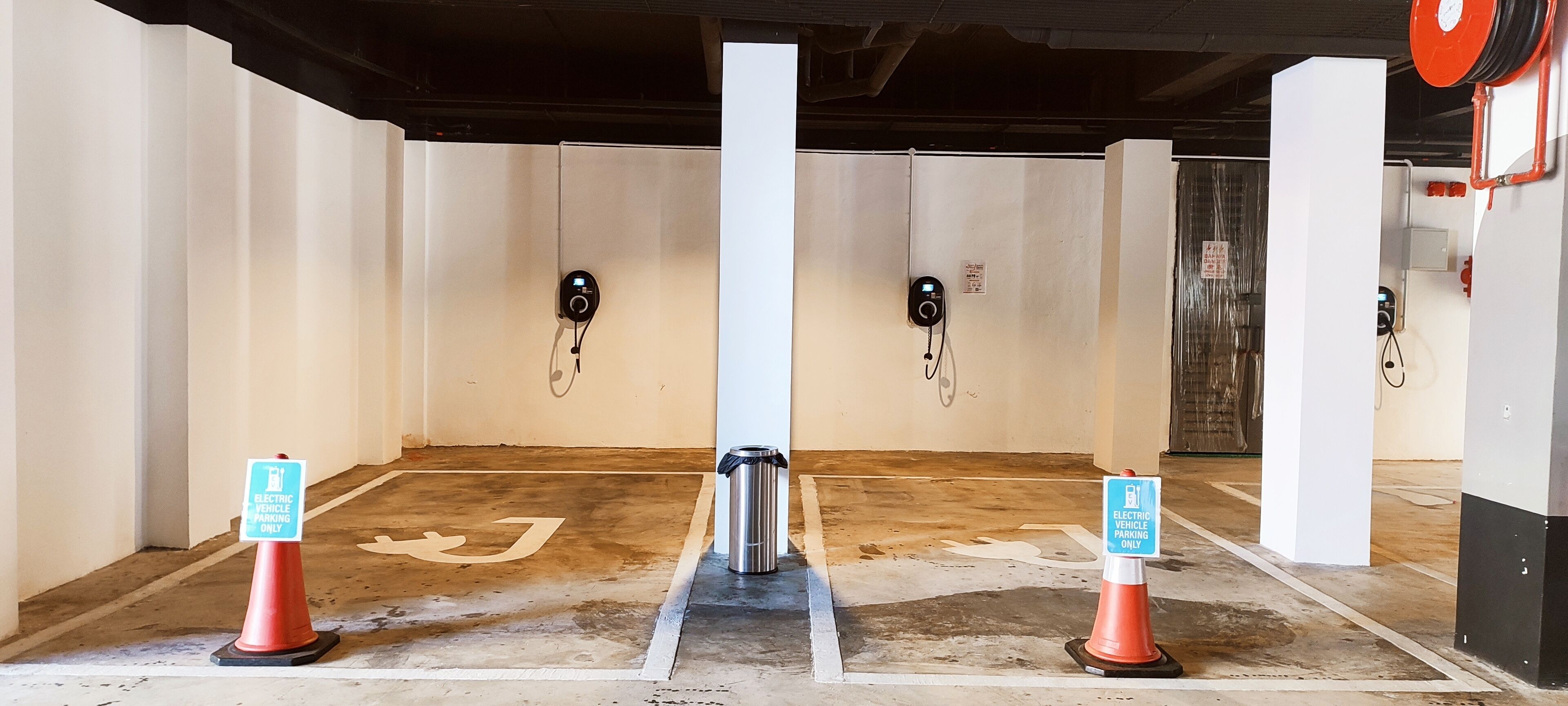 Un área de estacionamiento con estaciones de carga para vehículos eléctricos, señalizada con carteles y conos.
