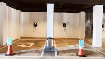 Un área de estacionamiento con estaciones de carga para vehículos eléctricos, señalizada con carteles y conos.