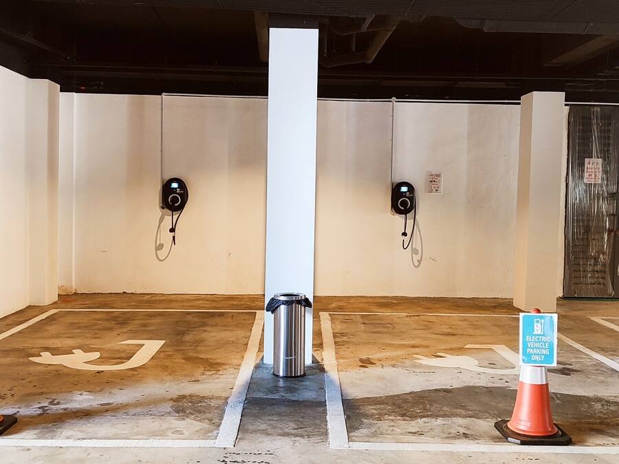 Un área de estacionamiento con estaciones de carga para vehículos eléctricos, señalizada con carteles y conos.