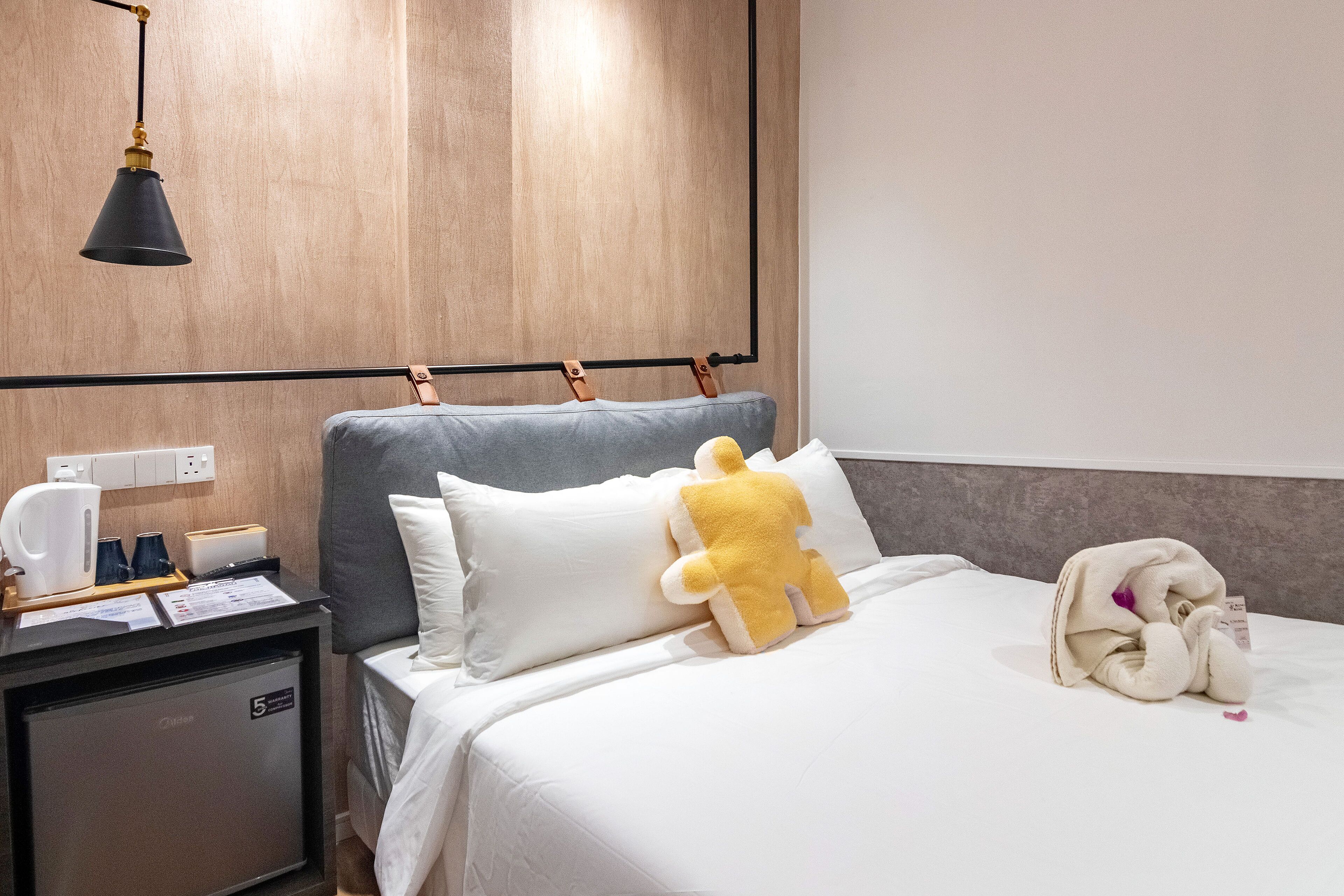 A hotel room with a bed, a nightstand, a desk, a lamp, and a wooden wall.