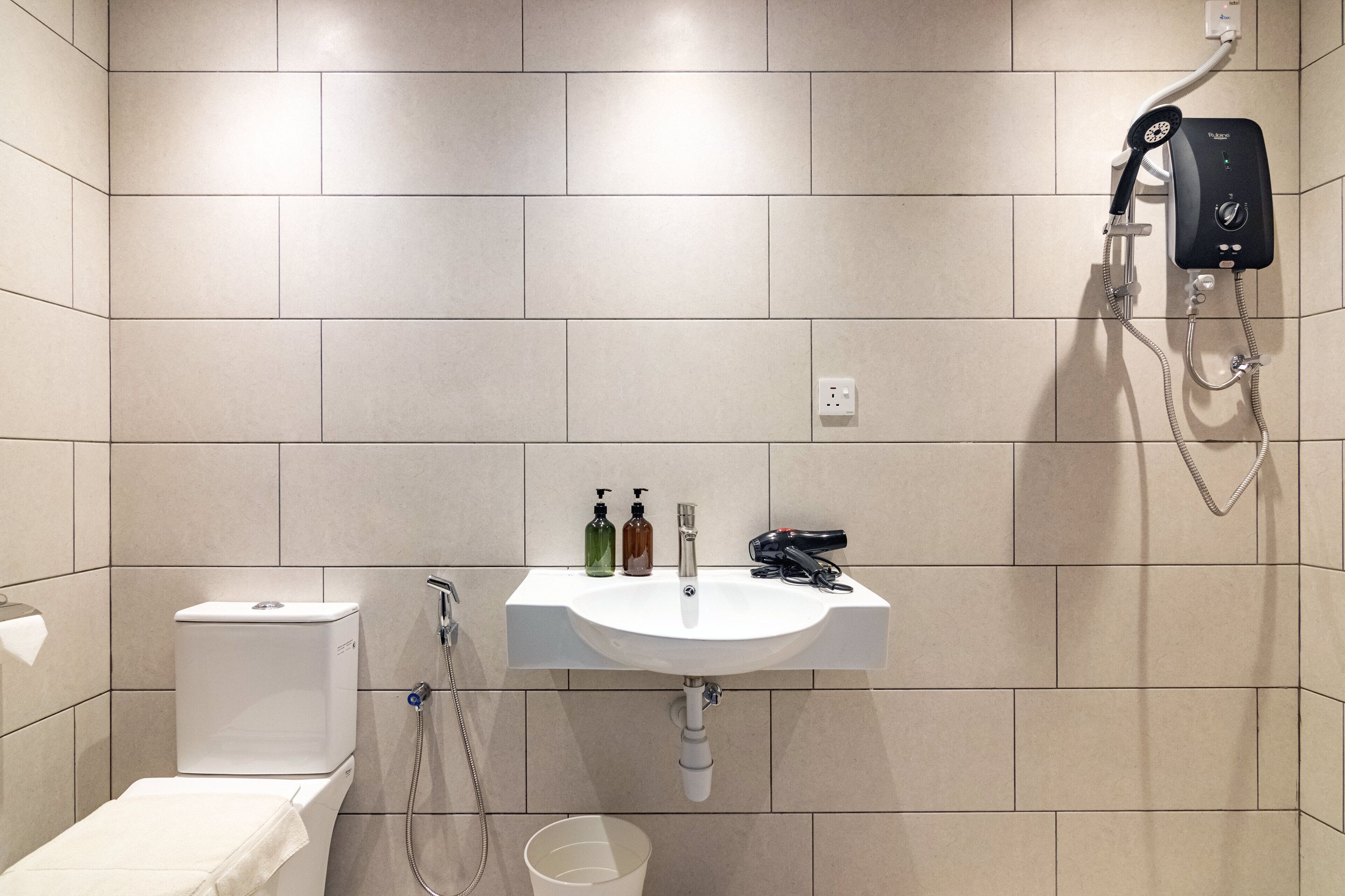 A bathroom with a white sink, toilet, and shower. There are bottles of shampoo and conditioner on the sink.